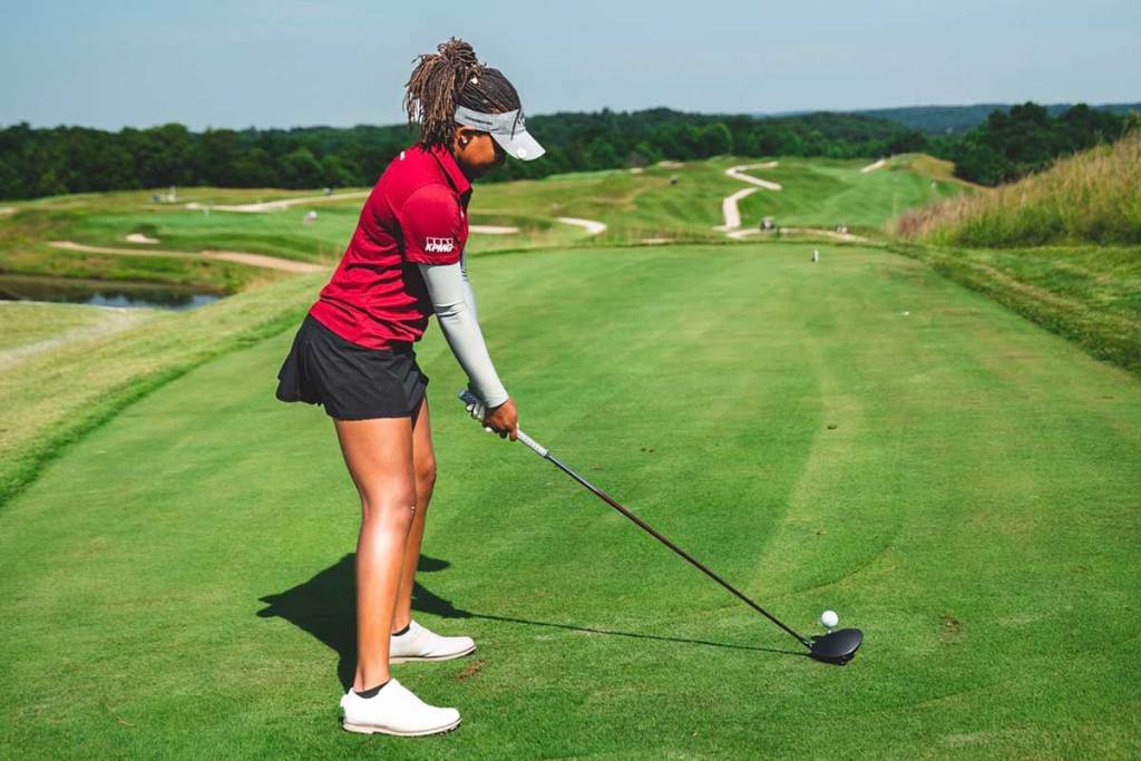 A woman in a red and black golfing outfit readies her golf club for a swing on the course.