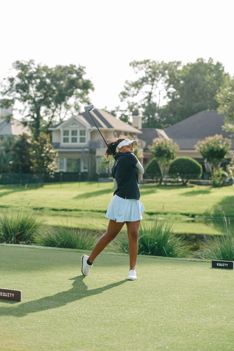 A woman swings on the golf course. Homes are visible beyond the edge of the course.