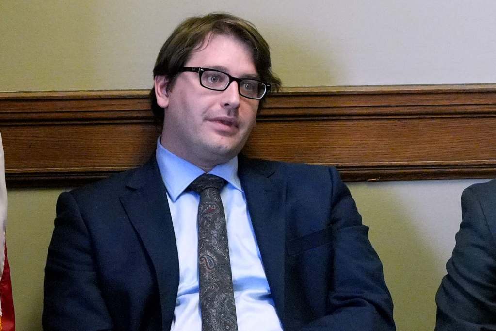A man in a suit seen seated, leaning against the wall