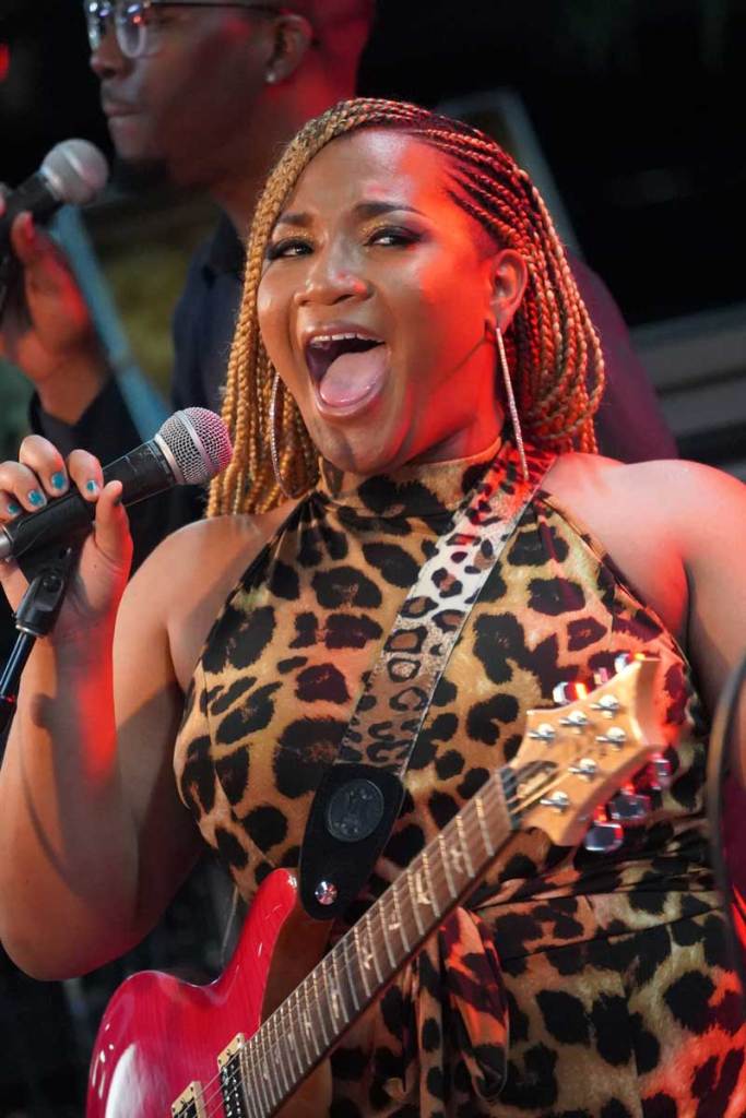 Closeup of a woman in a leopard print dress and a guitar strapped to her body, singing into the mic