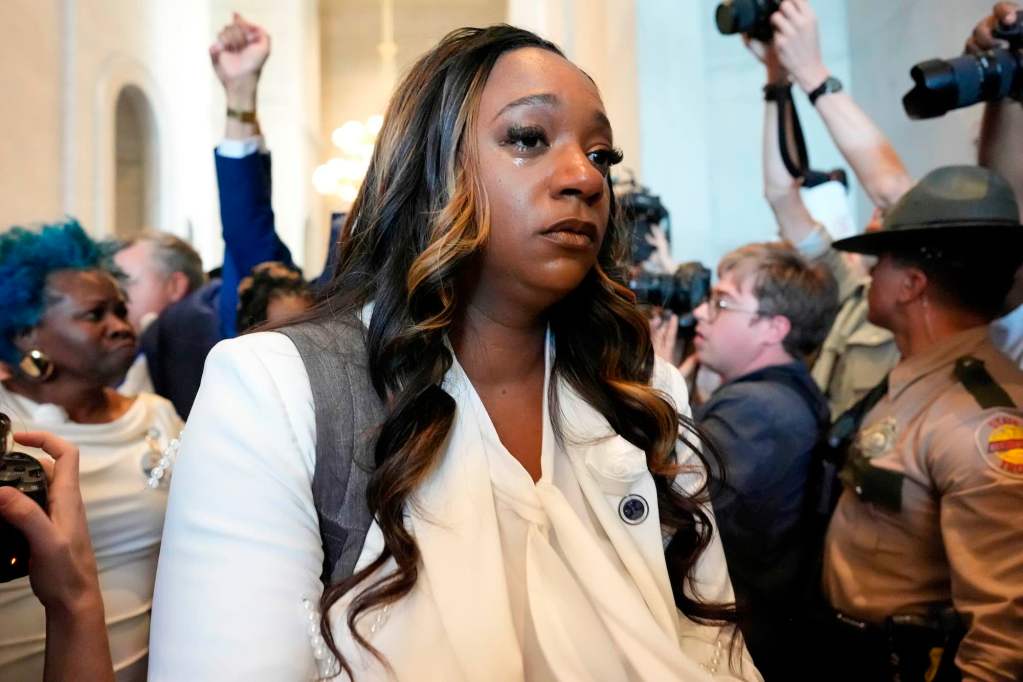 A black state representative is seen walking through a large crowd, tear running down her cheek as she leaves the senate chambers