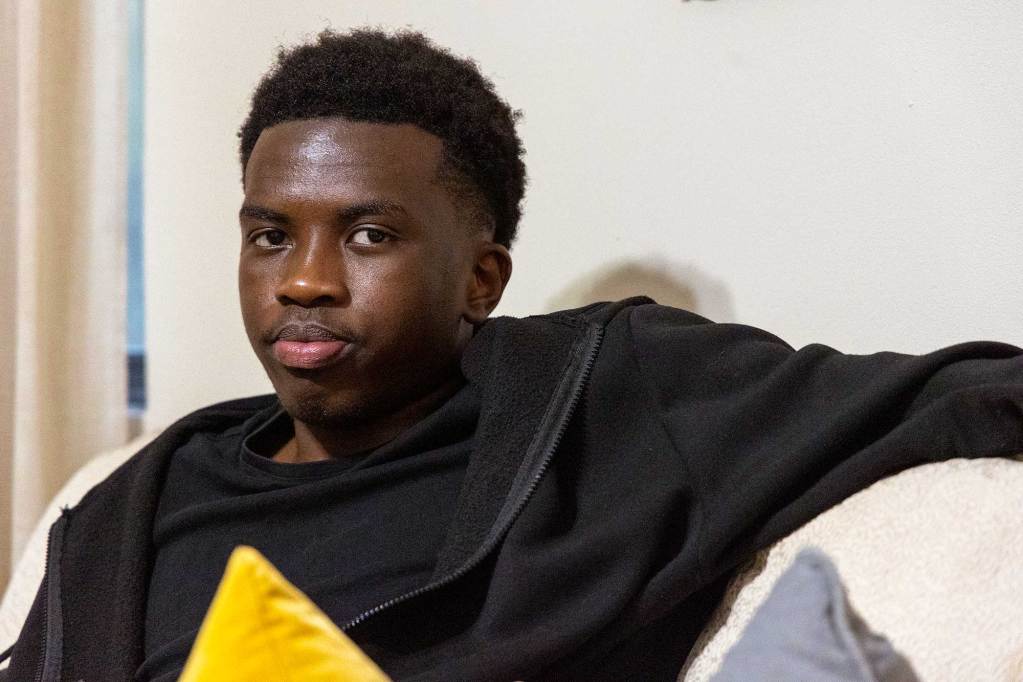 A closeup of Max Makoka, wearing black, seated on the couch inside the home