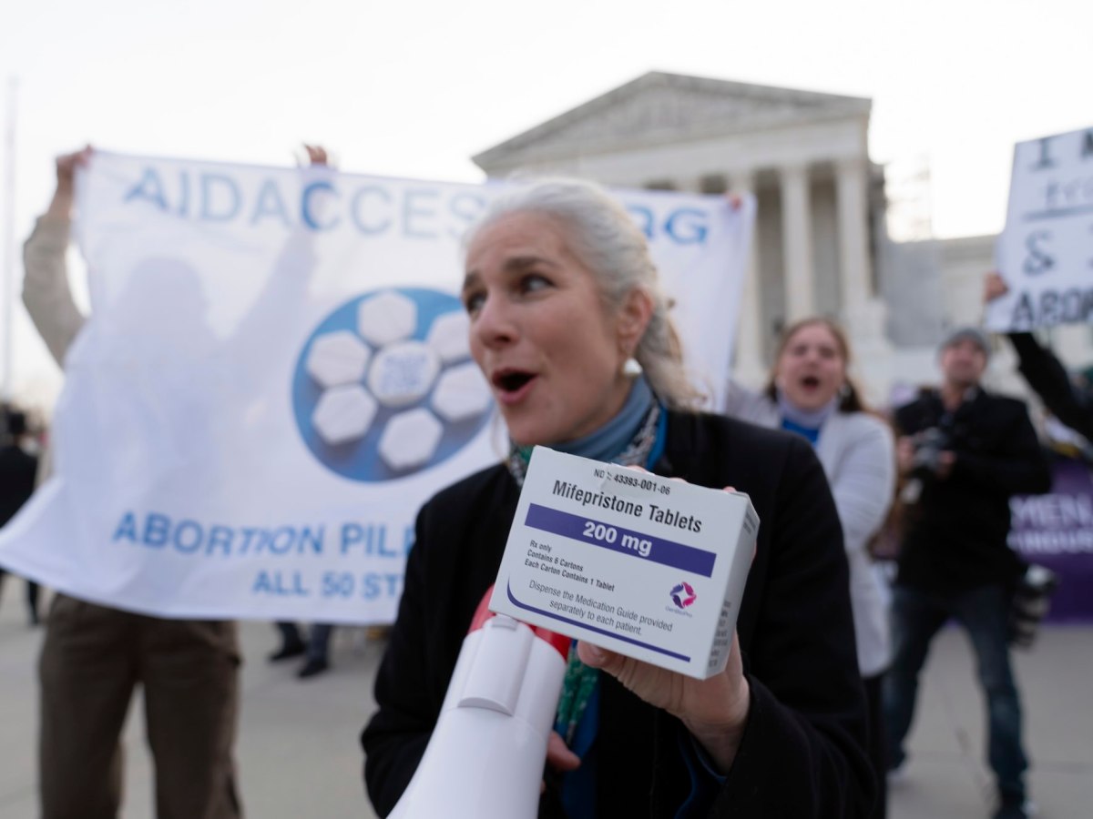 A person holds a box of mifepristone tablets in one hand and a megaphone in the other at an abortion rights rally
