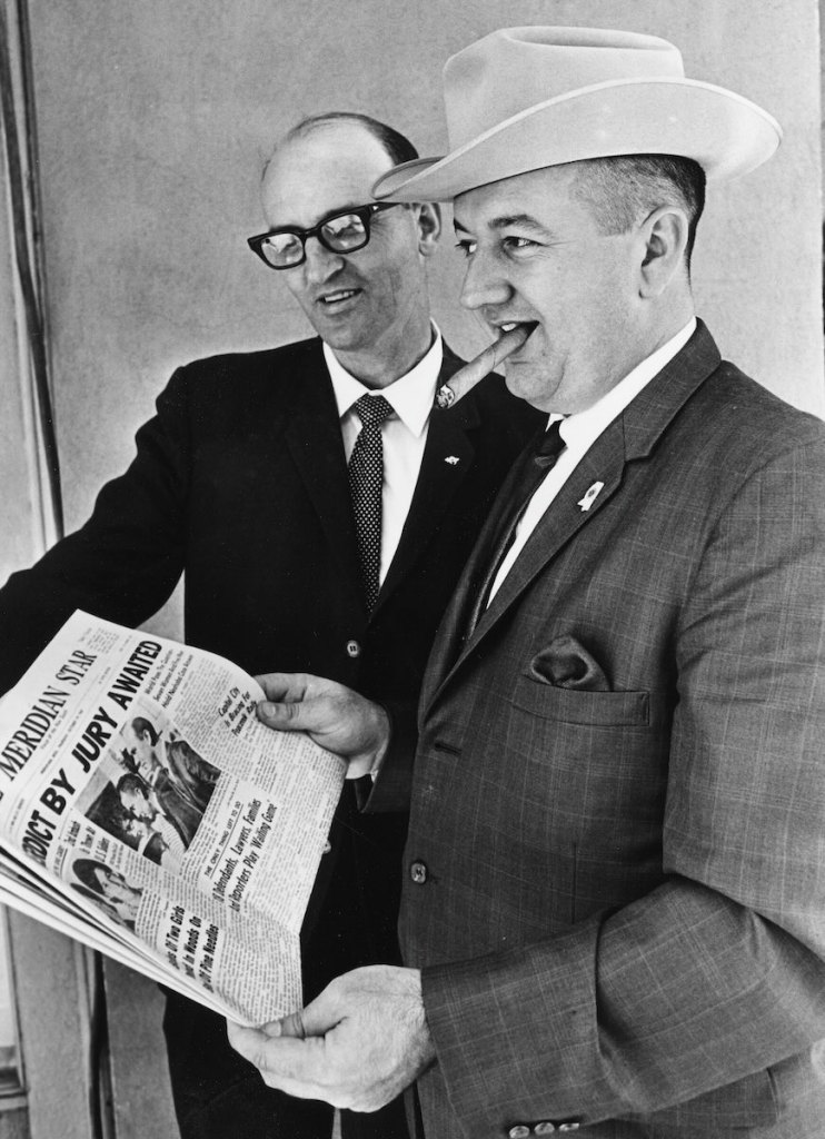 An old black and white photo from the 1960's of two men in suits holding up a newspaper with the headline 'Verdict by Jury Awaited'