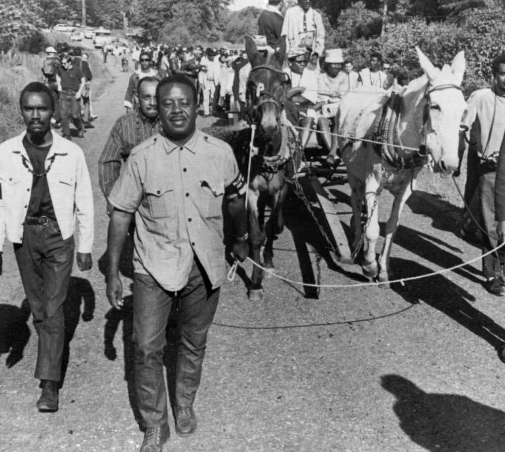 An old black and white photo from the 1960's showing marchers going down a road with a pair of mules