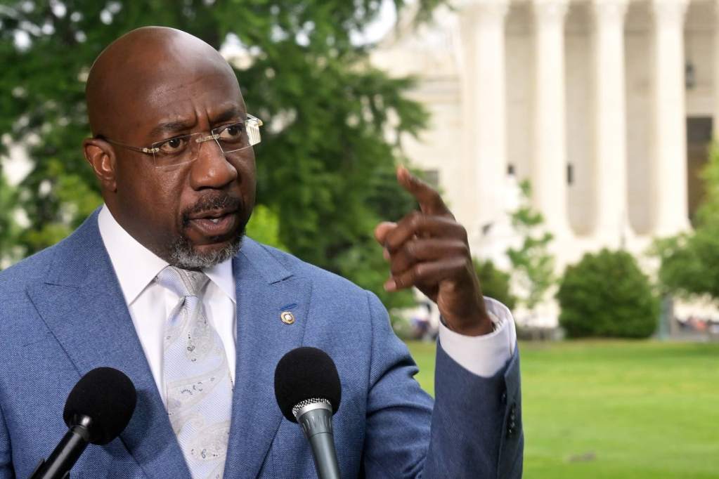 Raphael Warnock speaking at a podium outside