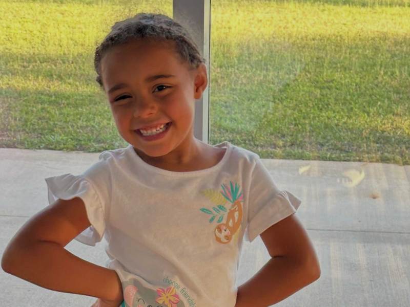 Ava Maie smiles while standing in front of a large window.