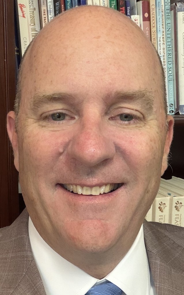 Bruce Case smiles for a headshot in front of a bookshelf.
