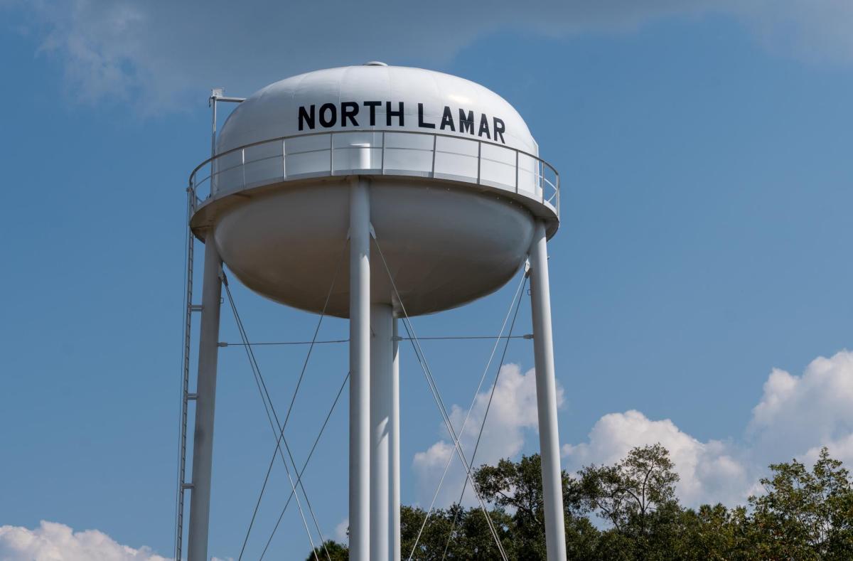 A white water tower as seen from the ground, with the name 'North Lamar' written on it in large black lettering