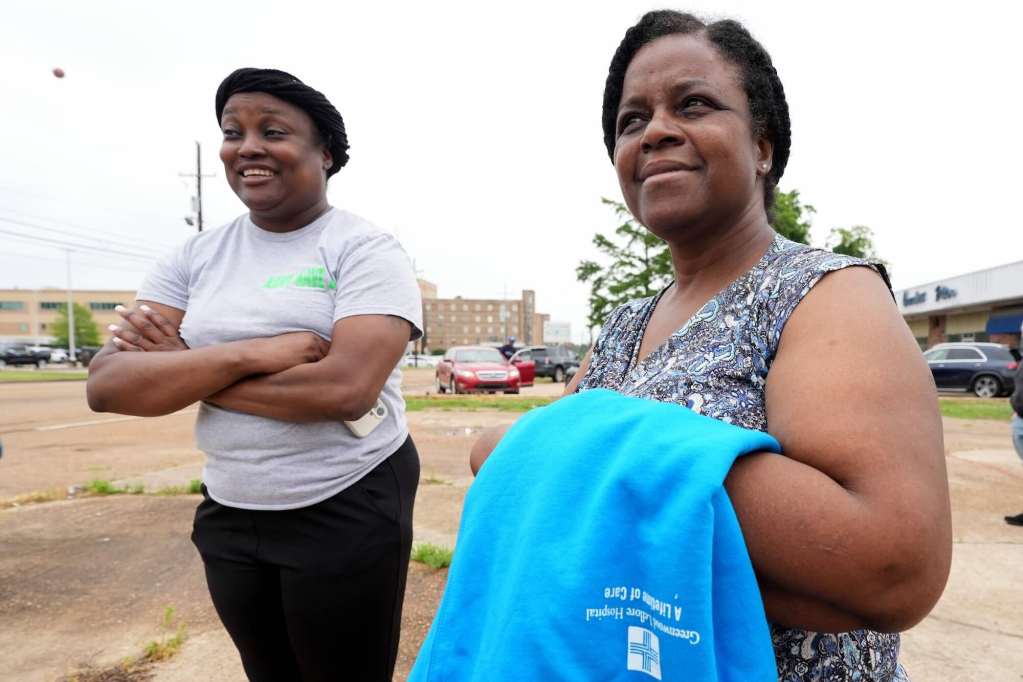 Two women stand in the parking lot outside of a hospital