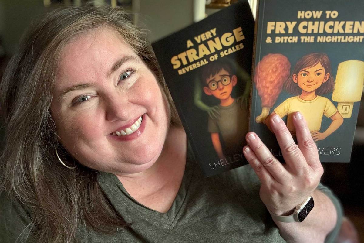 A woman with long brown hair smiles while holding up two books with illustrations on the covers. The titles are "A Very Strange Reversal of Scales" and "How to Fry Chicken & Ditch the Nightlight"