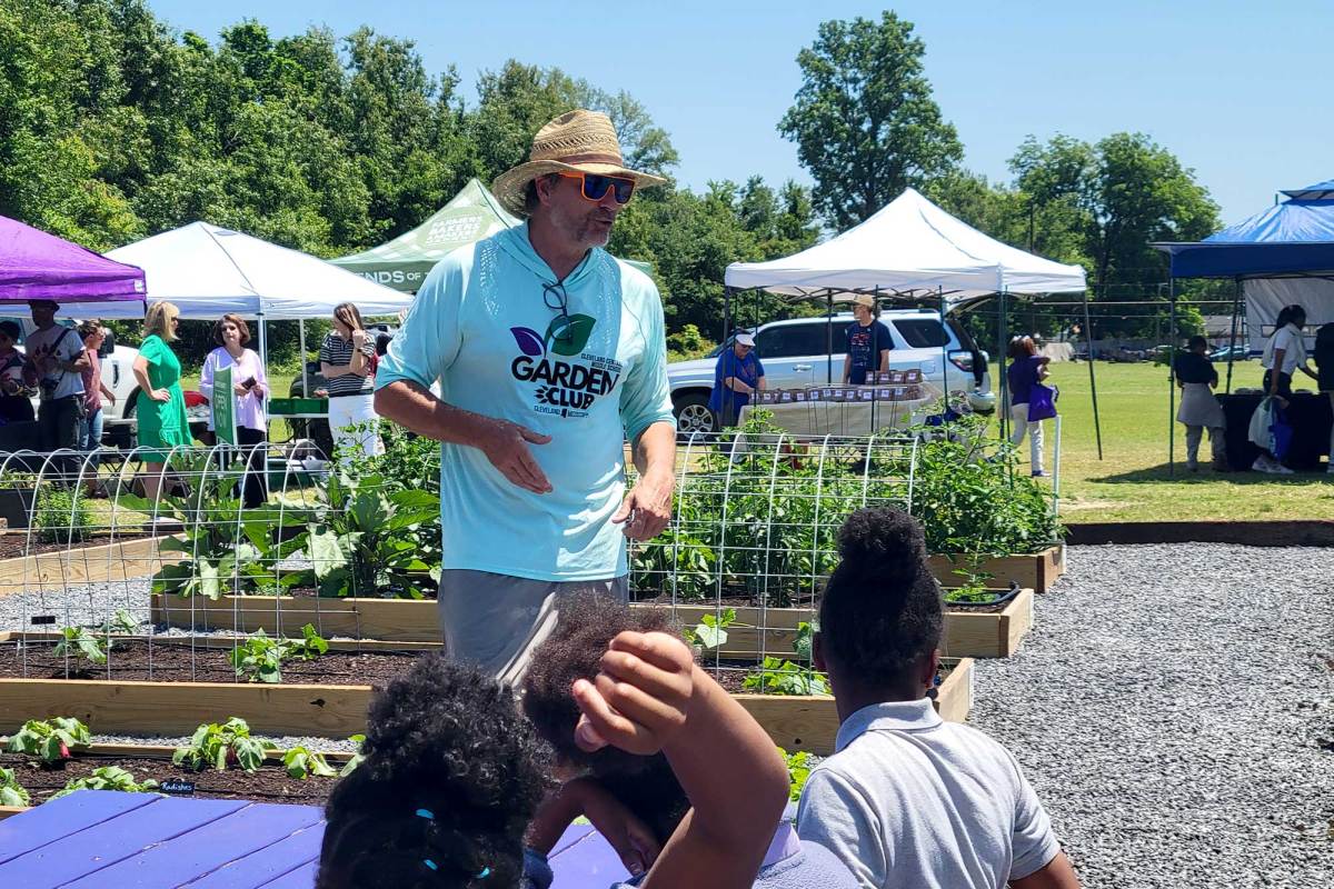 A man in a Garden Club tshirt speaks to students about the raised gardens beside them