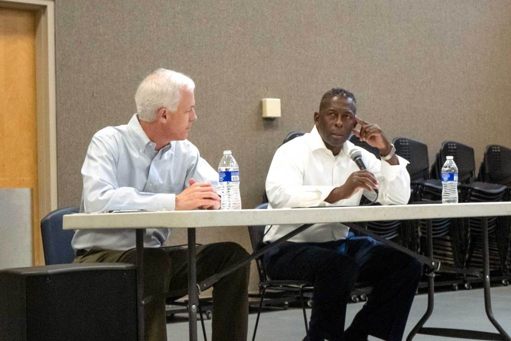 David Blount and Chris Bell speak to each other while seated at a table.