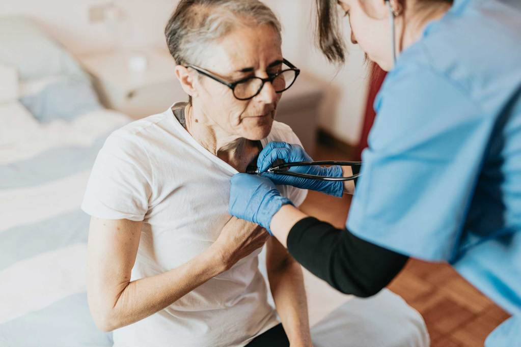 A female doctor using a stethoscope on an older woman.