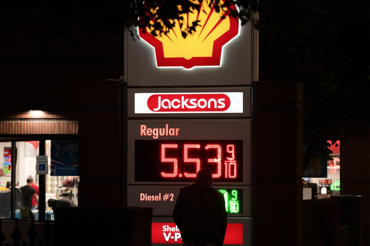 The silhouette of a man in front of a gas station display for gas prices.