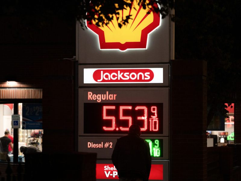 The silhouette of a man in front of a gas station display for gas prices.