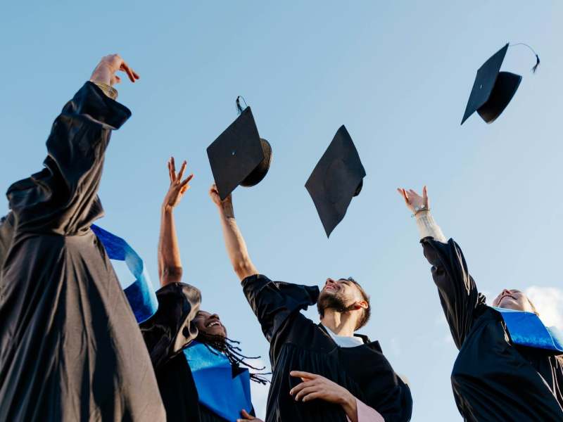 A group of students wearing graduation gowns throwing their caps into the air