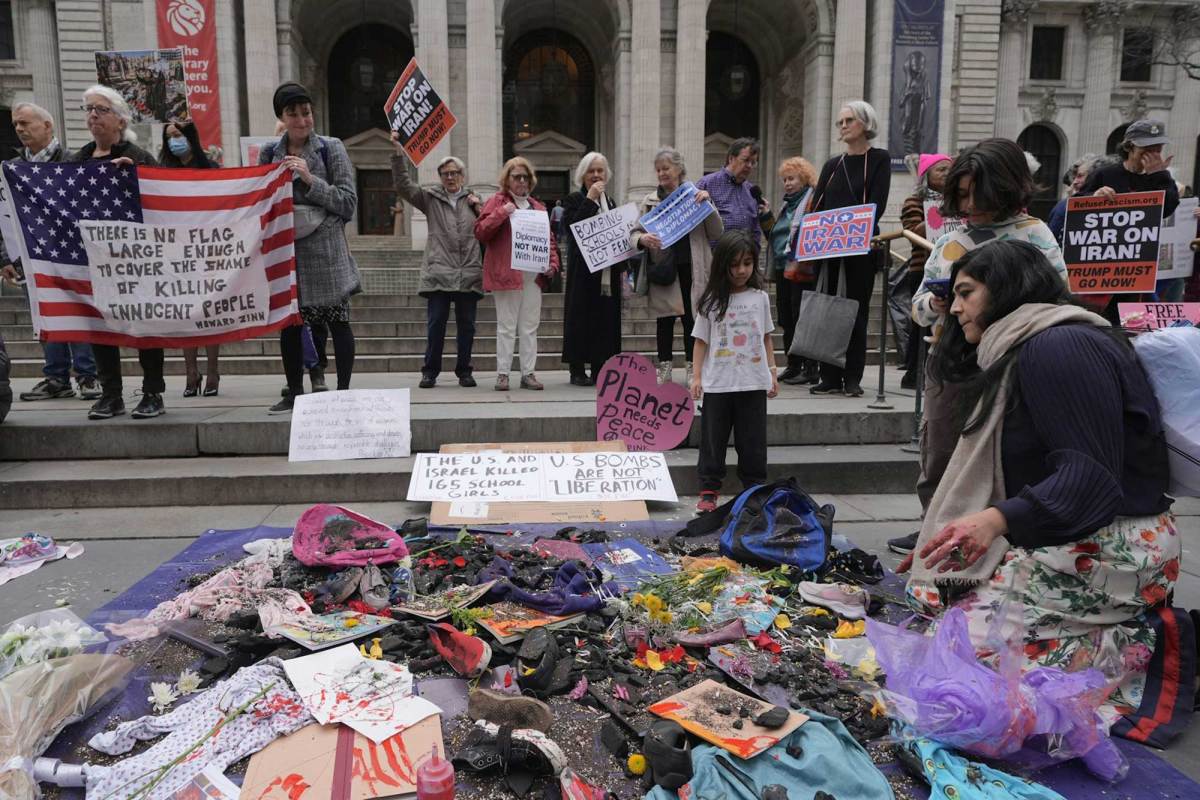 Protesters holding signs in front of a building. Before them is a pile of tattered clothes and belongings.