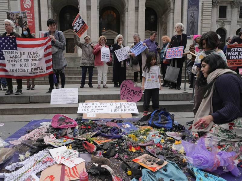 Protesters holding signs in front of a building. Before them is a pile of tattered clothes and belongings.