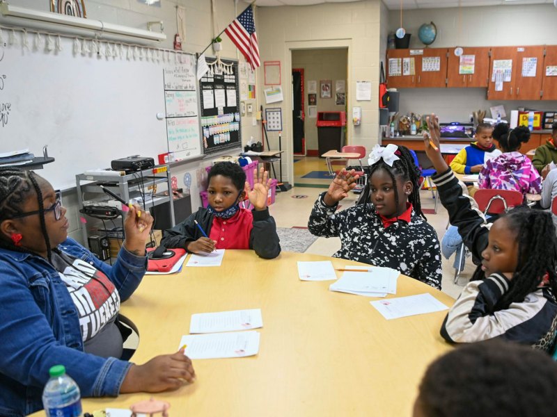 An elementary classroom, focusing on five students seated around a circular table with the teacher