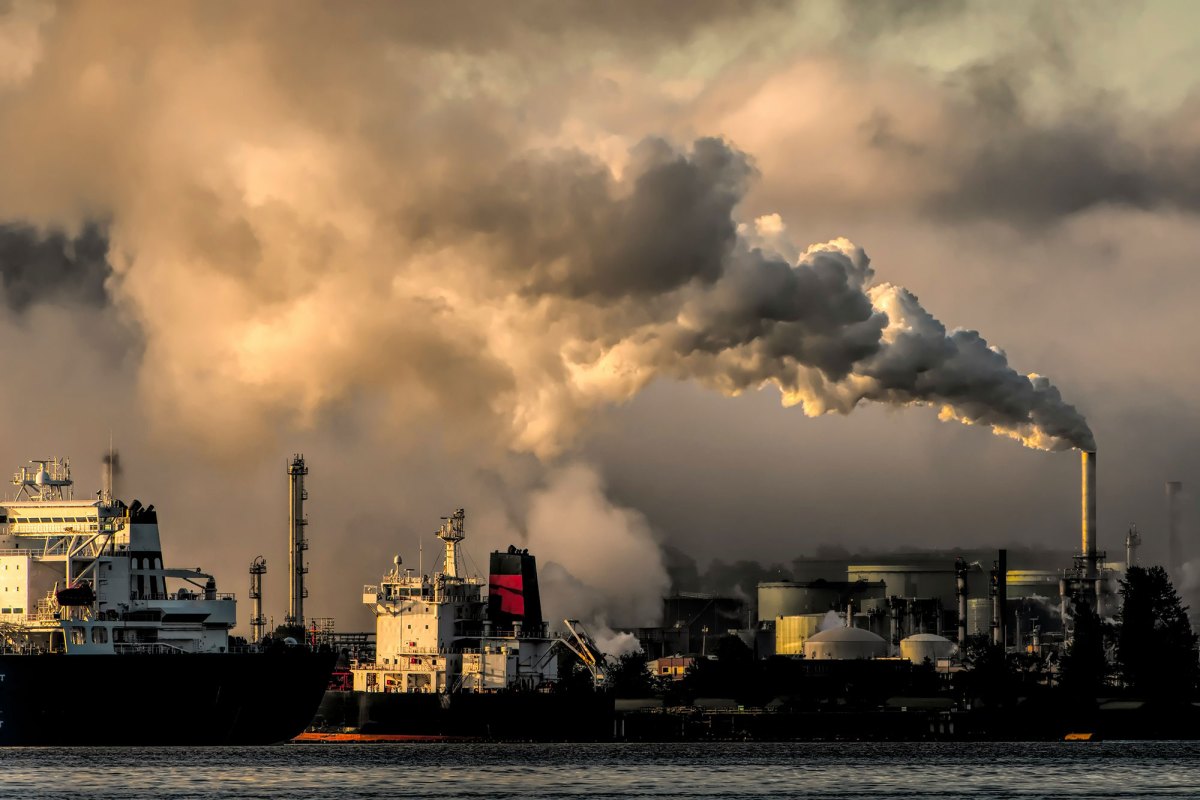 Smoke billowing from a smokestack at a port. Two ships are docked.
