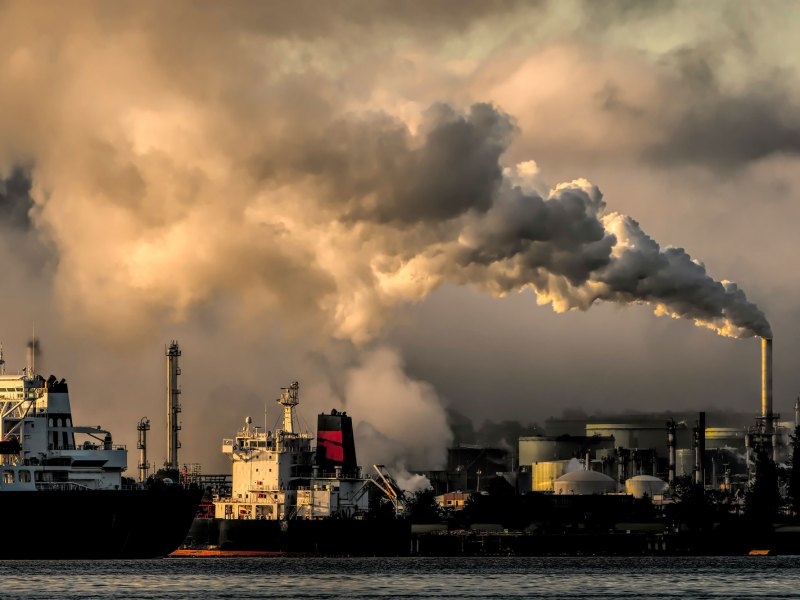 Smoke billowing from a smokestack at a port. Two ships are docked.