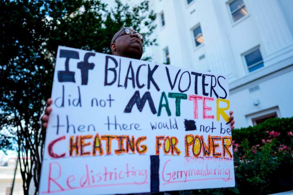 A person holding a sign that reads “If Black Voters did not matter, then there would not be cheating for power, Redistricting | Gerrymandering”