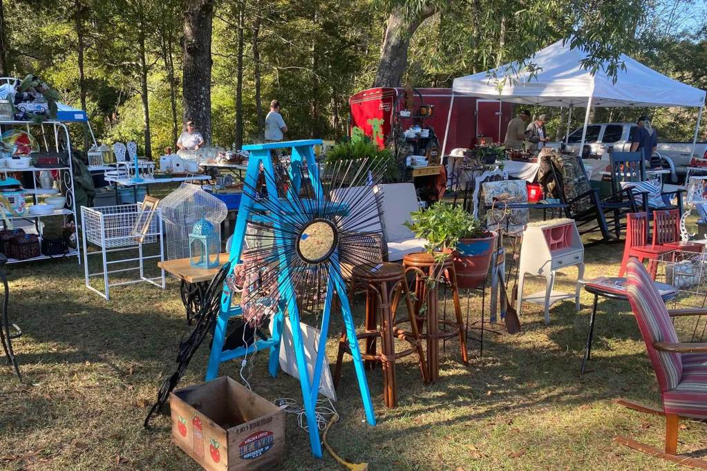 Tables and pop up tents set up for a yard sale outside in front of a wooded area