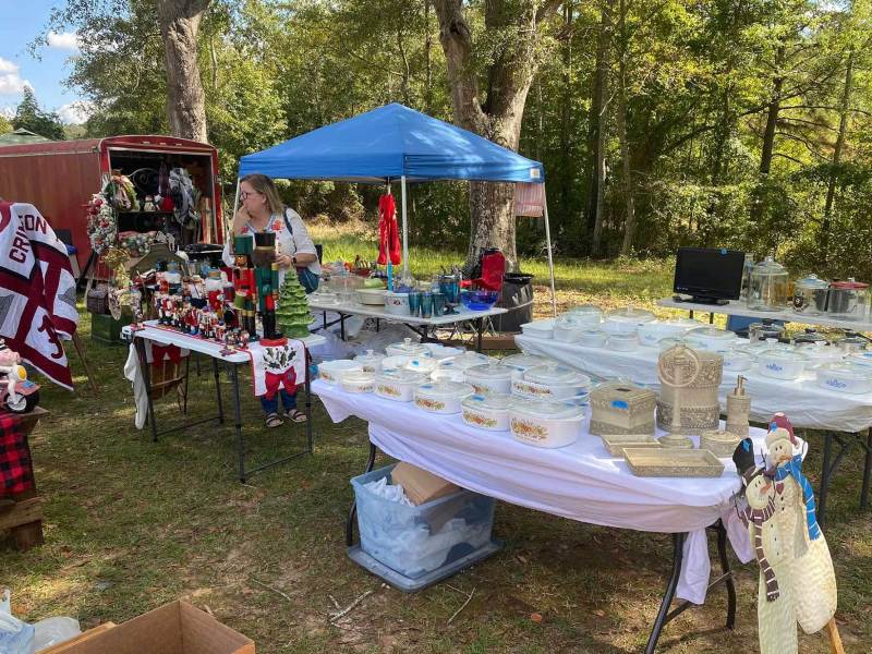 Tables and pop up tents set up for a yard sale outside in front of a wooded area