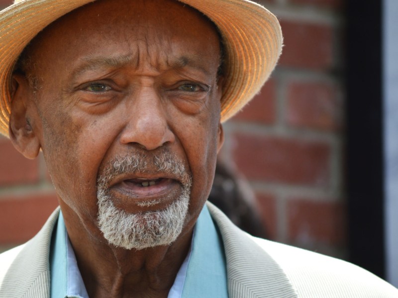 A closeup of Bo Brown, wearing a hat, standing outside a red brick building