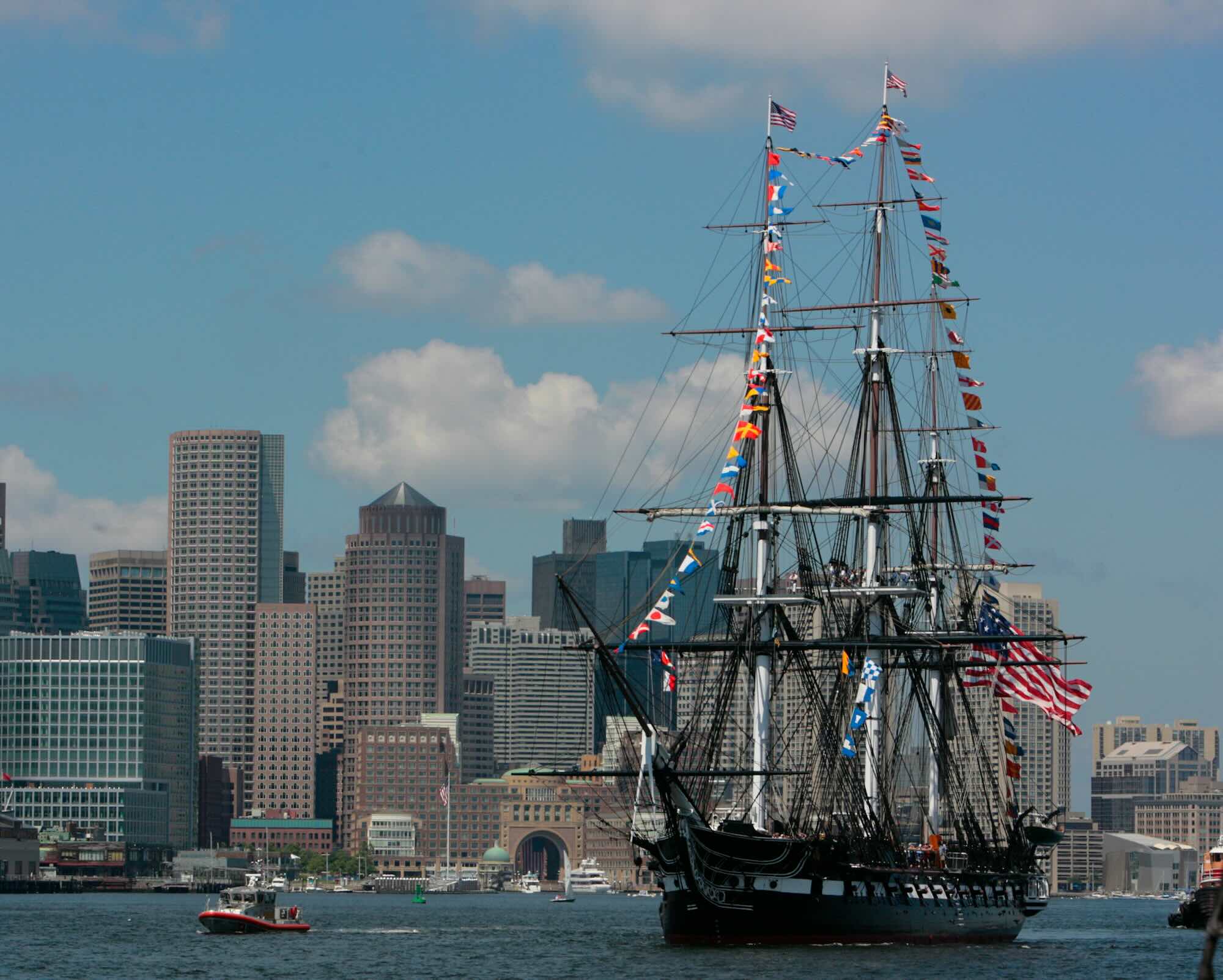A large boat with tall masts on the water with a city in the background.