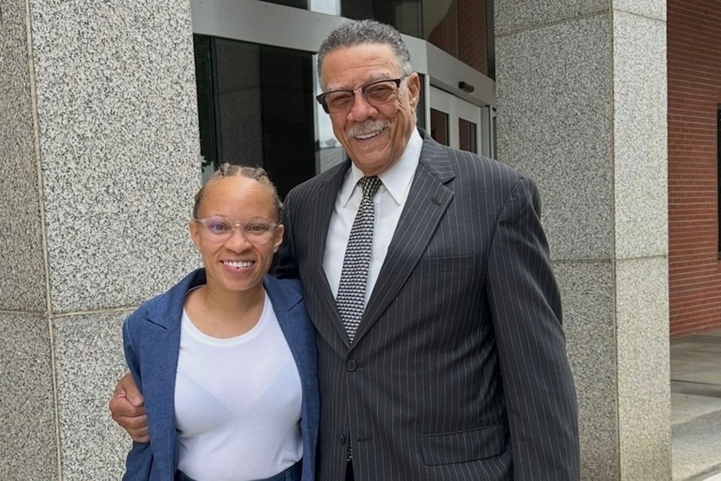 A photo shows a smiling Black woman in a blue pantsuit next to a smiling Black man in his 80s wearing a dark gray suit.