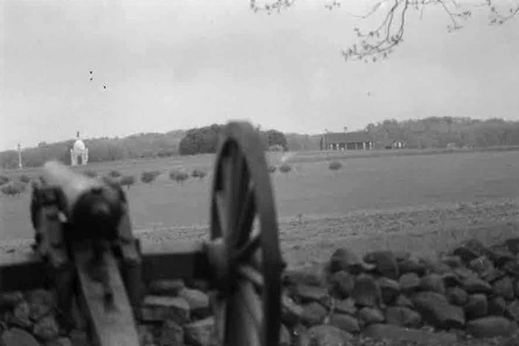 A black-and-white photo of a mobile cannon with an empty field in the background.