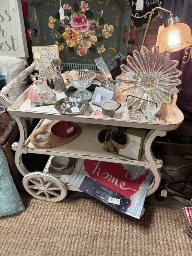 A flea market display of kitchen ware and decor on a wheeled white tea table