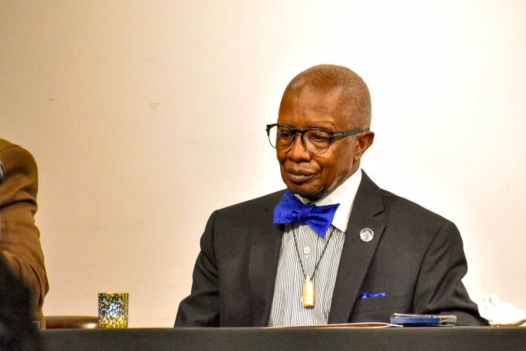 Sen. Hillman Frazier, in grey suit and cobalt blue bowtie, sits at an event