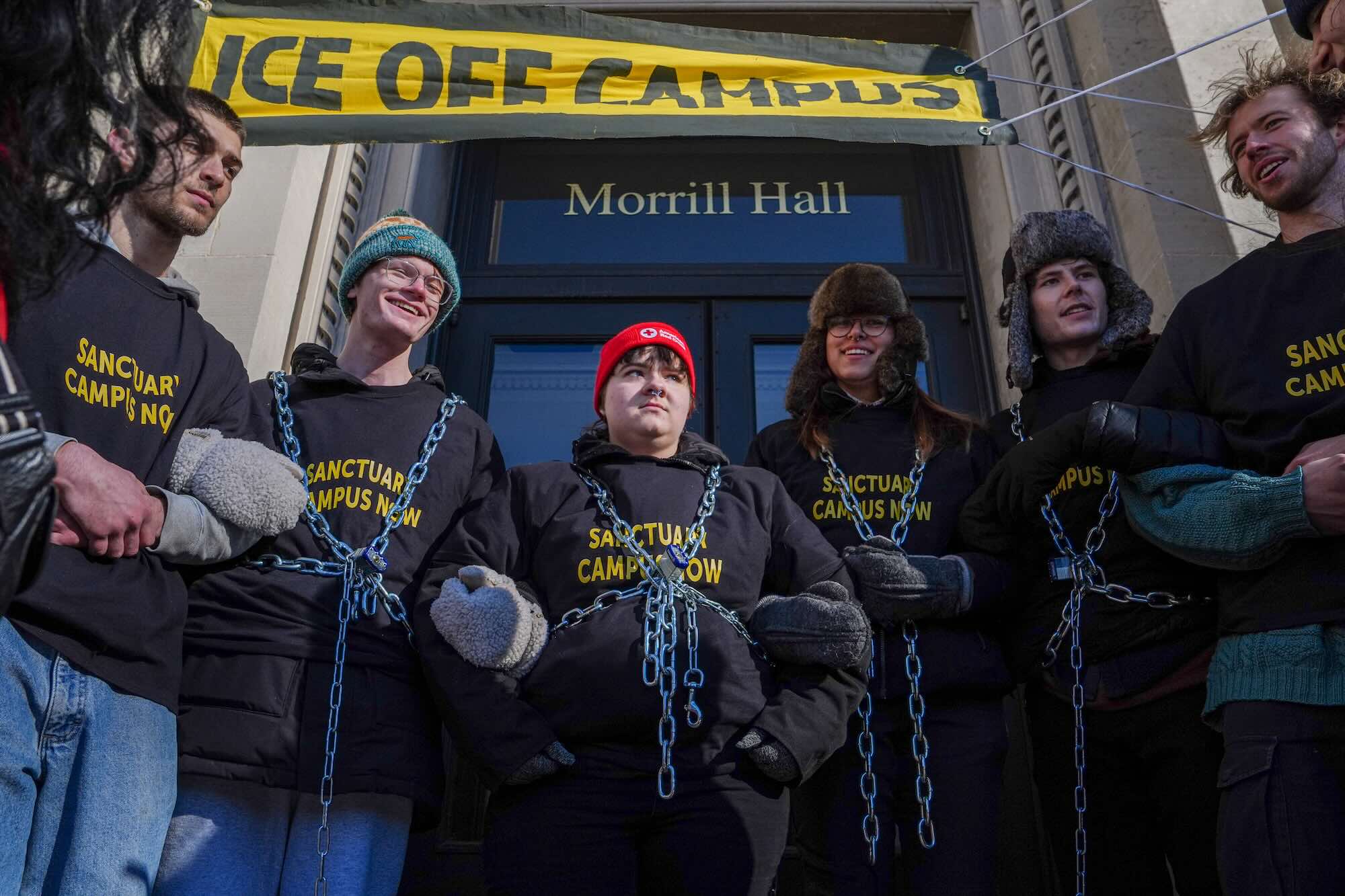 FIve people lined up and each wearing chains in front of a building.