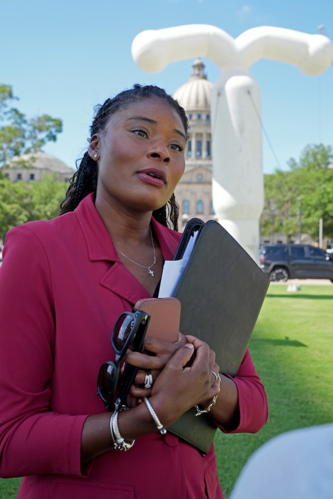 Kamesha Mumford stands outside, a large white inflated IUD seen in the background