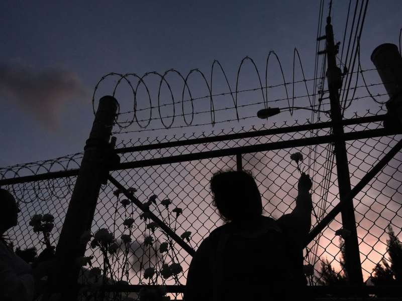 A woman placing a flower on a fence topped with barbed wire.