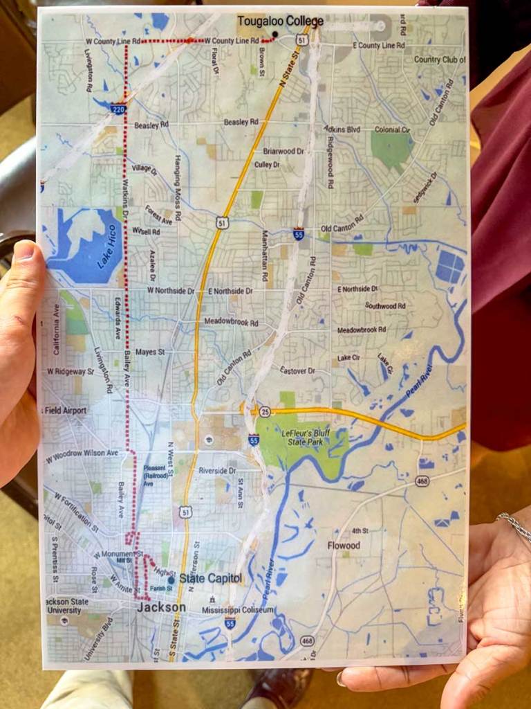 A hand holds up a large print of a map showing a march path between Tougaloo College and the Jackson capital building