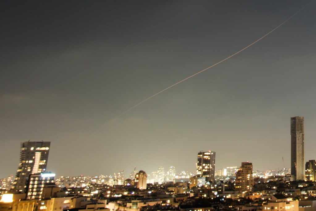 A orange streak in the sky over a busy city at night