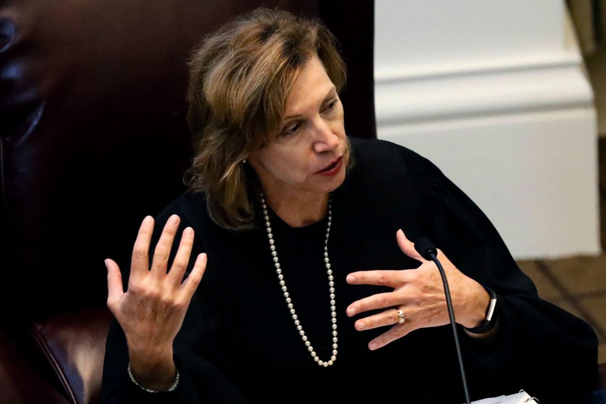 A judge in robes sits and speaks at her desk