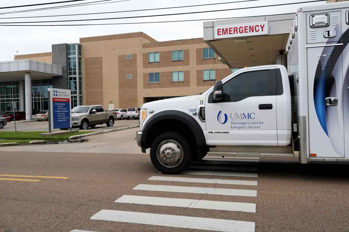 A light brown brick building labeled Greenwood Leflore Hospital, with a UMMC Emergency Services vehicle driving past