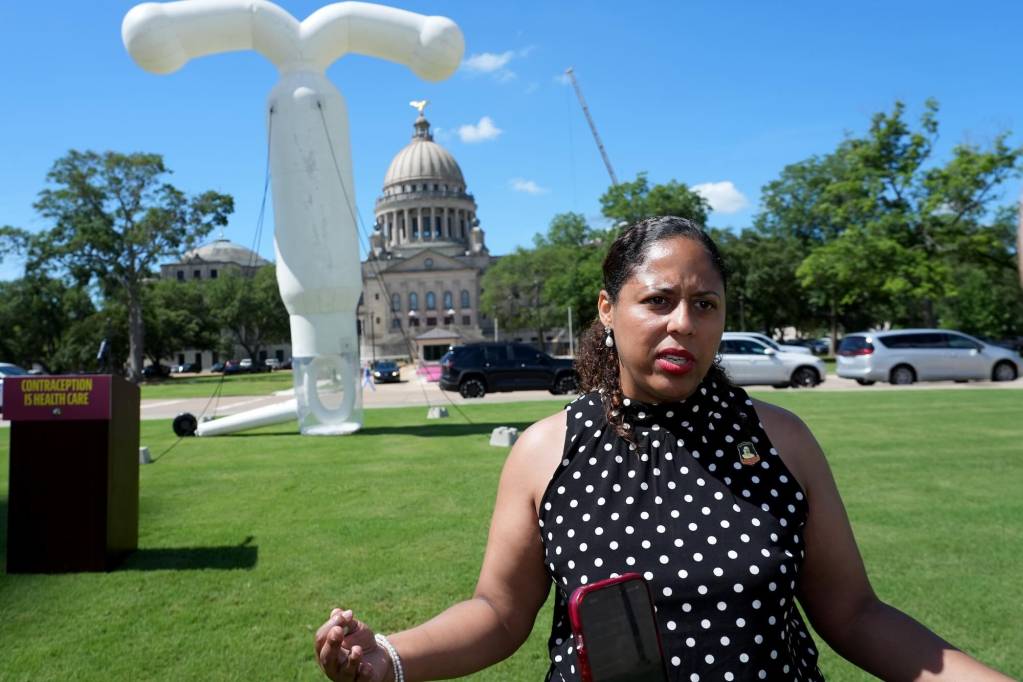 Zakiya Summers speaks outside on the lawn of the Mississippi capital building. A large white inflated IUD stands behind her.