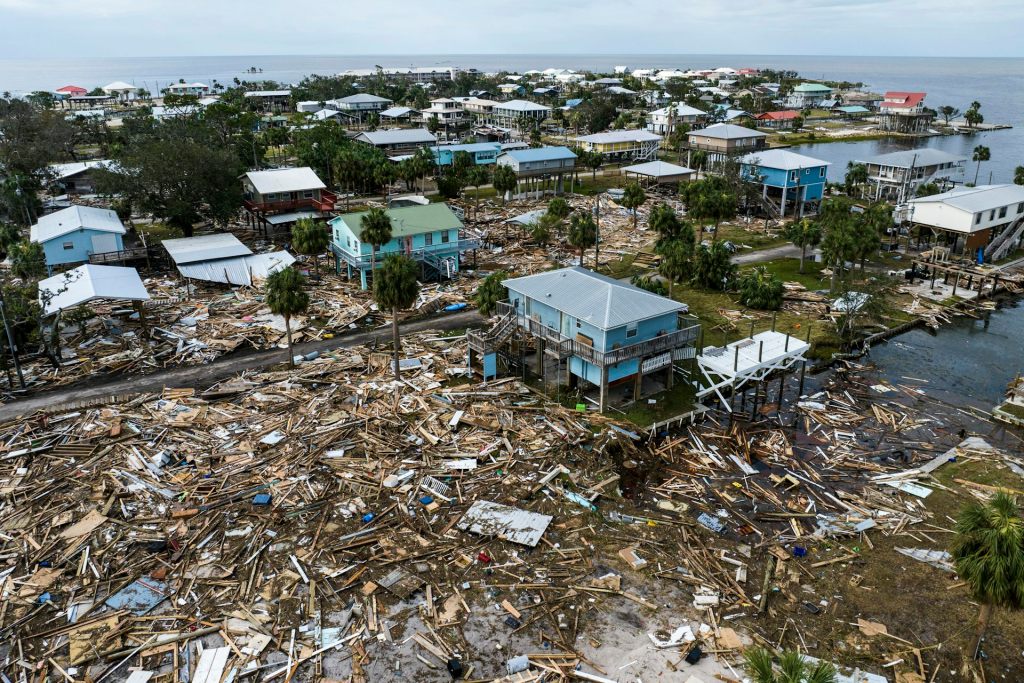 Debris and damage homes across a town with the Gulf waters in the background