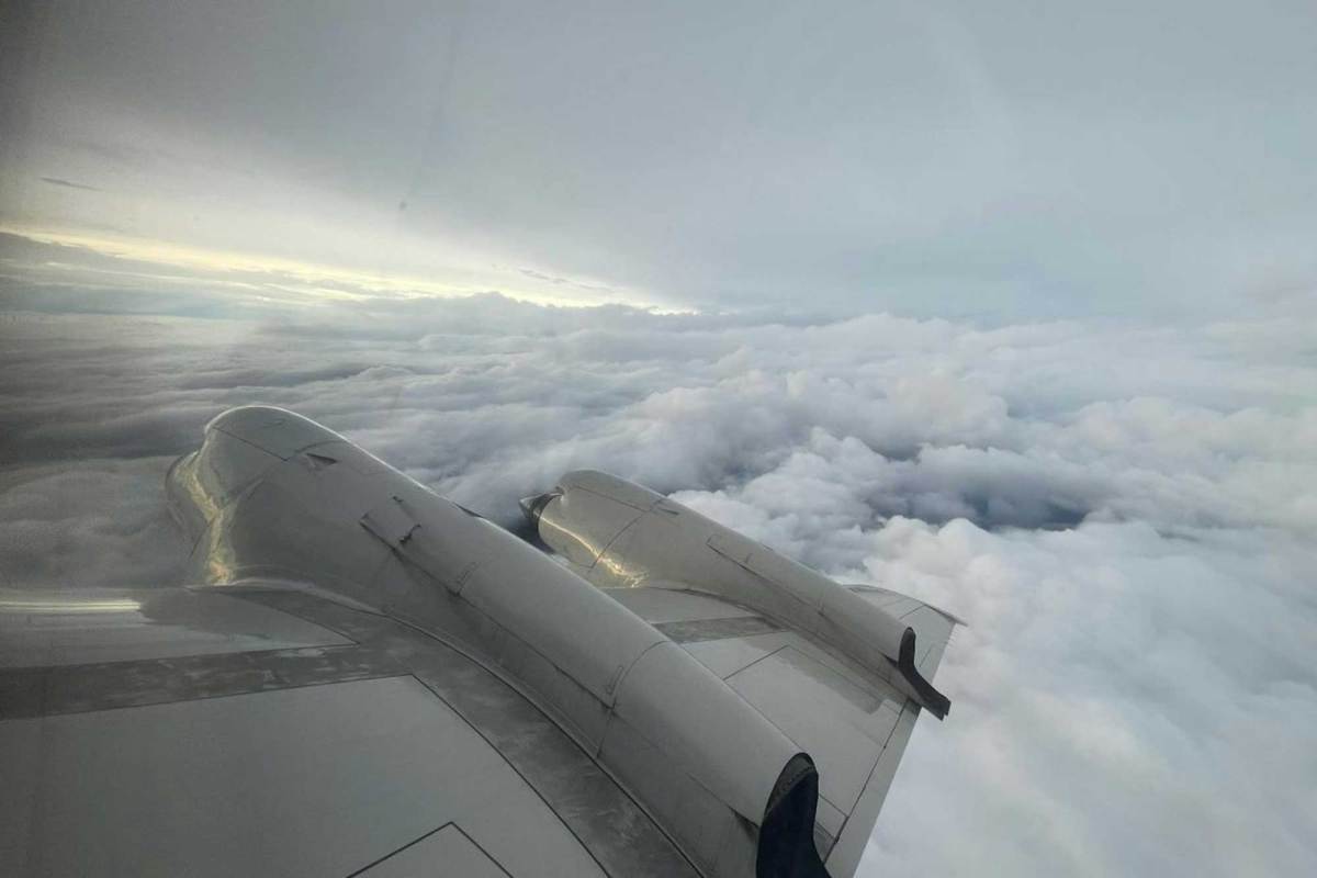 A view of a plane wing from inside the plane, flying over a hurricane cloud.